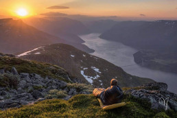 a person sitting on a hill looking at a river